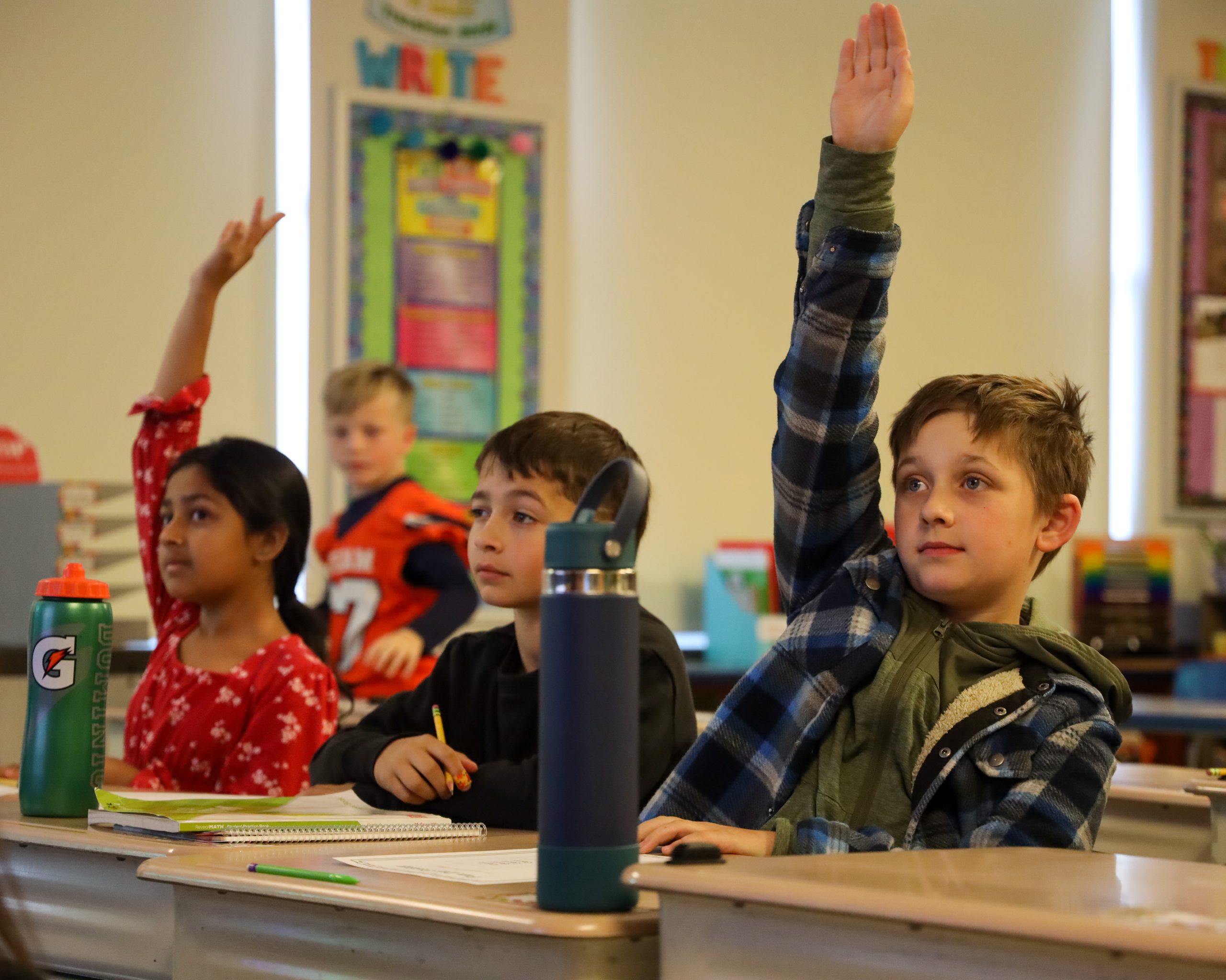 Elementary students in class, raising their hands during a lesson 