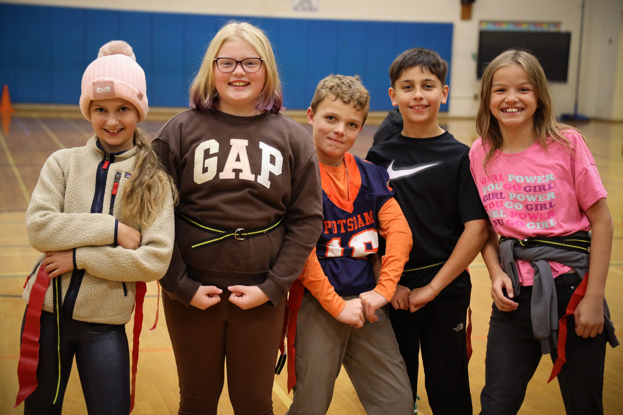 Middle school students smile at the camera in their flag football gear during gym class.