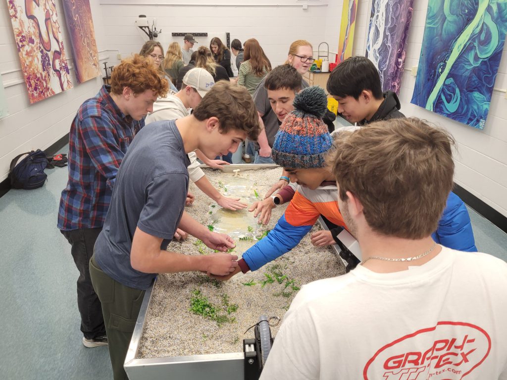 Students gather  around model of a river.
